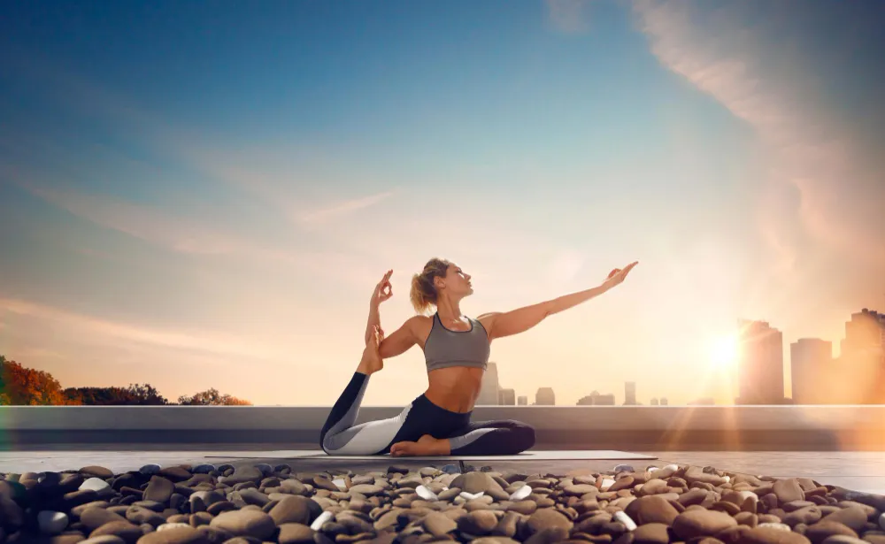 woman in sportswear doing a yoga stretch on a rooftop at sunrise, representing that girl body wellness and morning energy