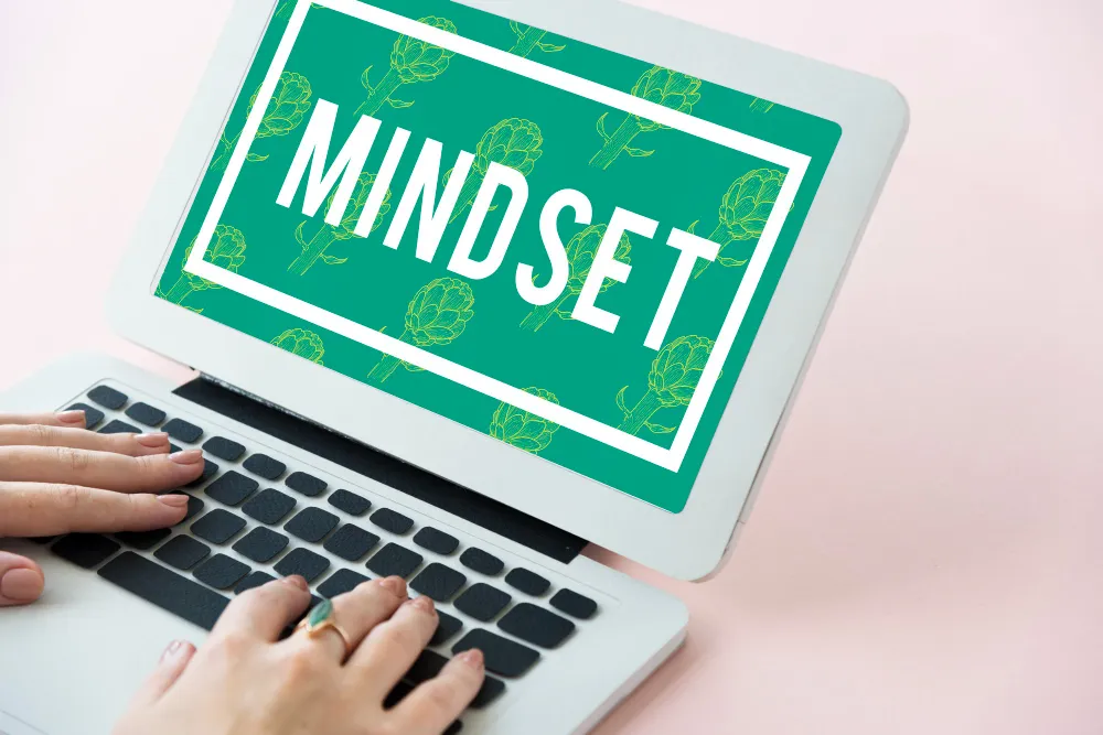 hands typing on a laptop with a green screen that says mindset, highlighting that girl growth-focused mindset and identity work
