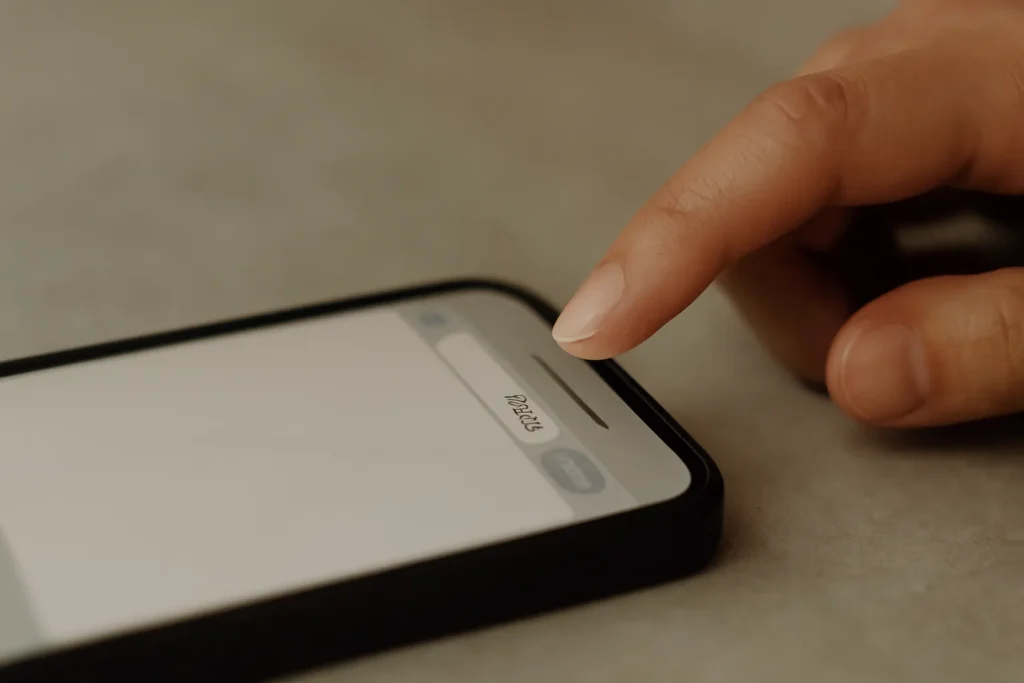 Close-up of a hand hovering above a smartphone’s reply box on a neutral surface (1600×900).
