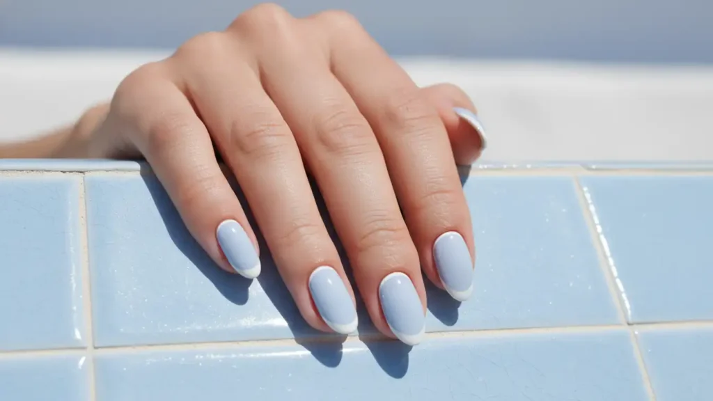 Pastel blue manicure with two blue tones on almond nails resting on soft blue knitted fabric.
